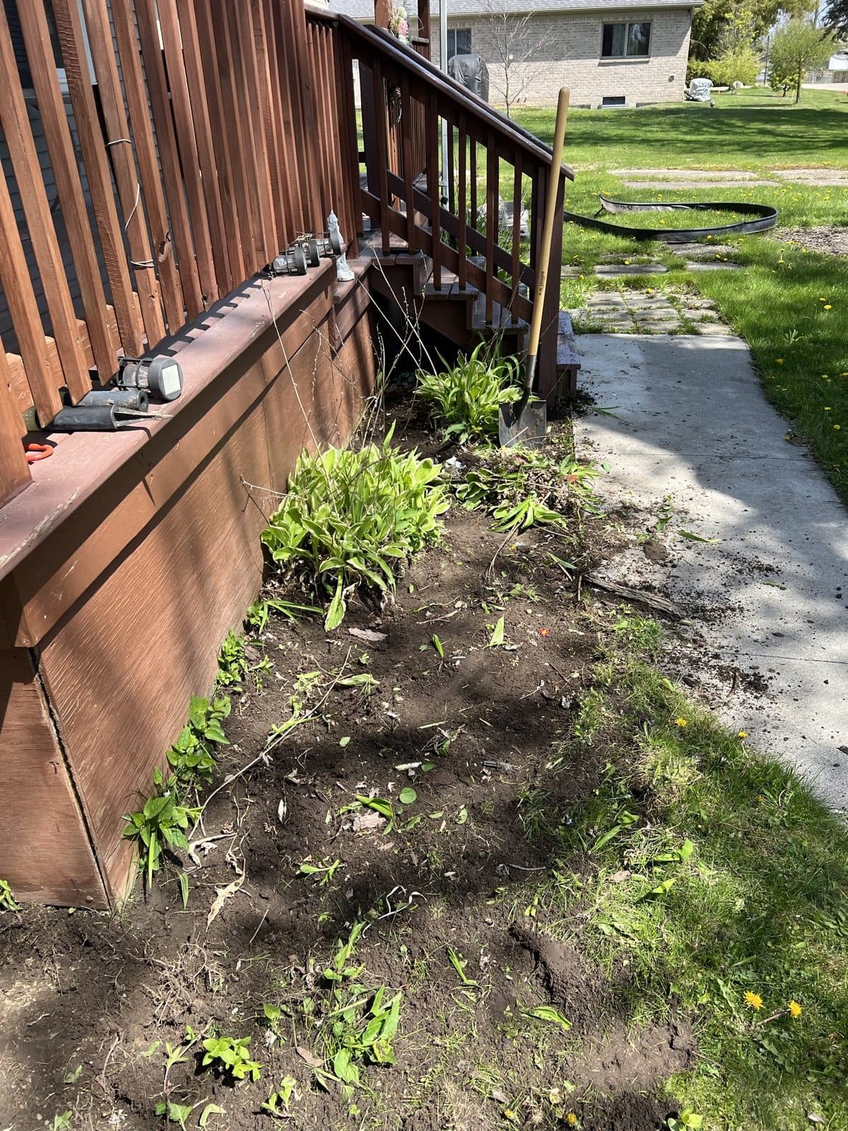 A bare dirt garden bed running along a backyard deck before the work