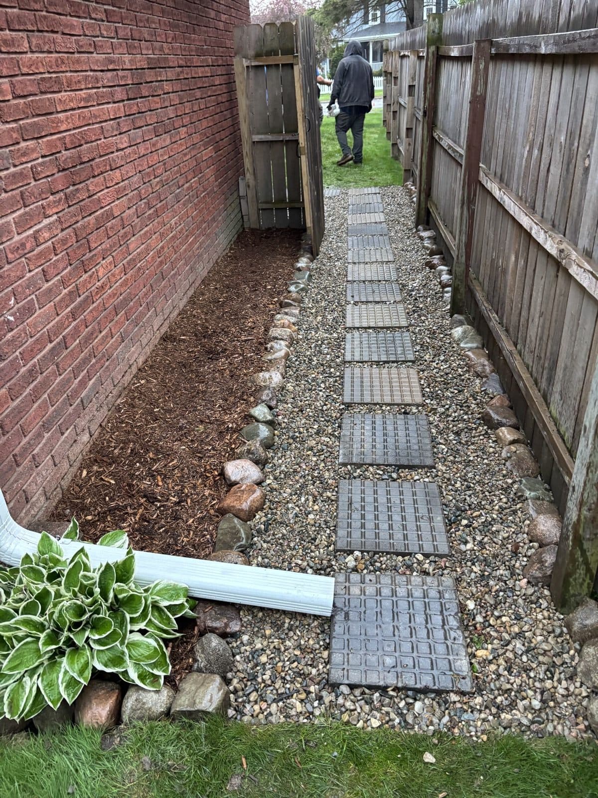 Paver stone walkway running along a brick wall and wood privacy fence down the side of a house